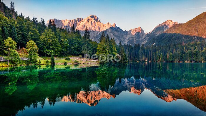 Bild Calm morning view of Fusine lake. Colorful summer sunrise in Julian Alps with Mangart peak on background, Province of Udine, Italy, Europe. Beauty of nature concept background.