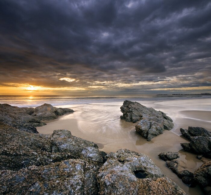 Bild Felsen am Strand bei Sonnenaufgang mit dramatischen Himmel