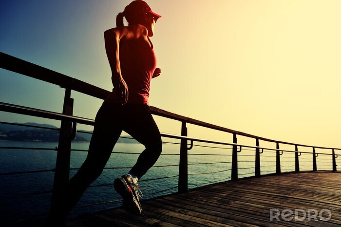 Bild junge Fitnessfrau, die auf Sonnenaufgang-Strandpromenade läuft