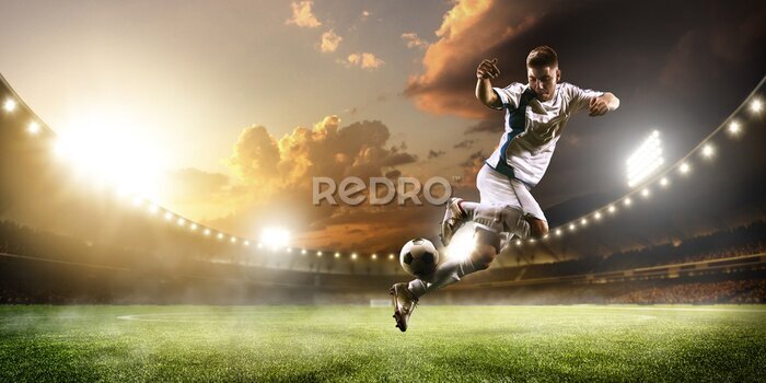 Fototapete Ein Fußballspieler in Aktion in einem Stadion mit Flutlicht