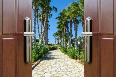 Fototapete Eine offene Tür führt zu einem palmengesäumten Gehweg