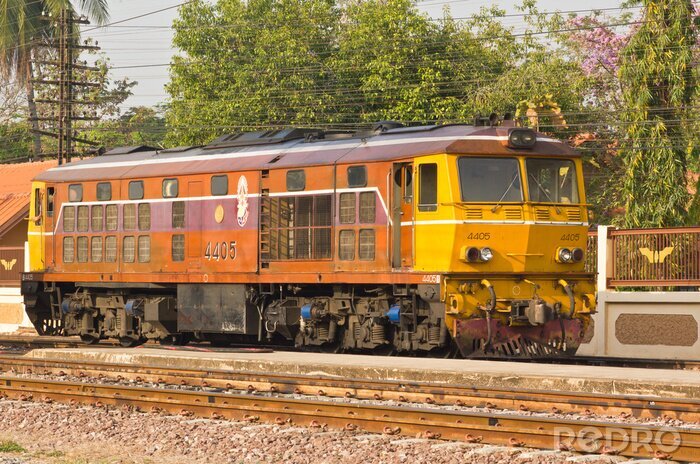 Fototapete Gelb-orangenfarbener Zug auf Gleisen