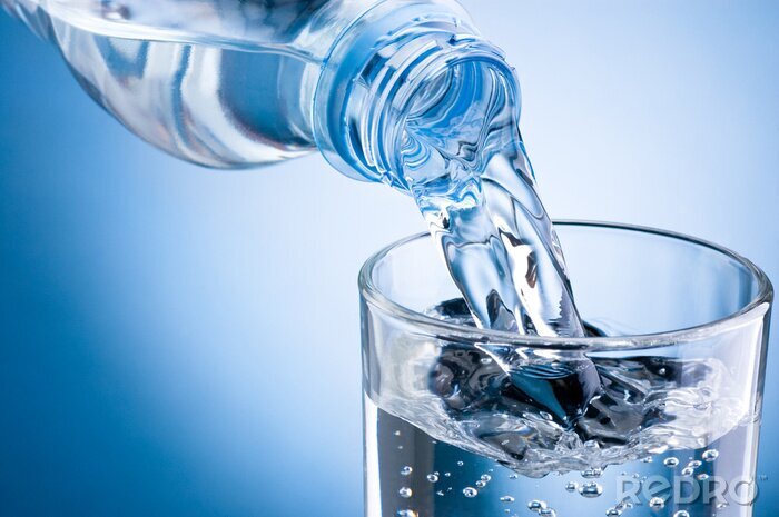 Fototapete Gießen von Wasser aus Flasche in Glas auf blauem Hintergrund