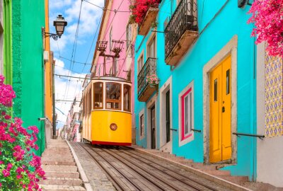 Fototapete Lisbon, Portugal - Yellow tram on a street with colorful houses and flowers on the balconies - Bica Elevator going down the hill of Chiado.