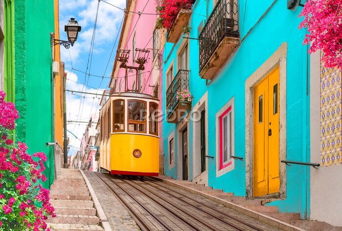 Fototapete Lisbon, Portugal - Yellow tram on a street with colorful houses and flowers on the balconies - Bica Elevator going down the hill of Chiado.
