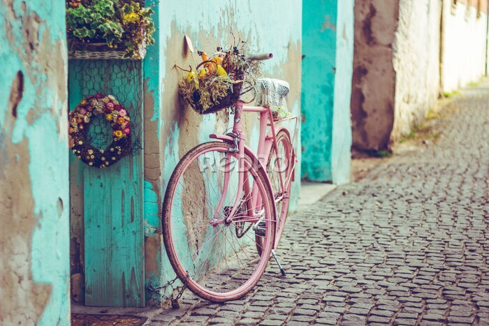 Fototapete Pink vintage bike with basket full of flowers next to an old cyan building in Spain