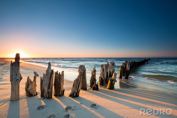 Fototapete Sonnenuntergang am Ostseestrand und altes hölzernes Wellenbrecher