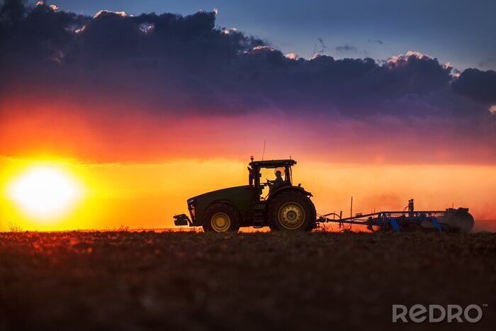 Fototapete Traktor arbeitet bei Sonnenuntergang