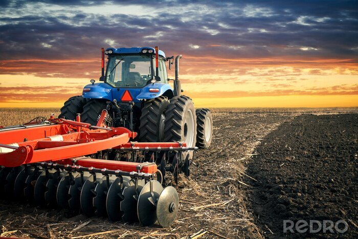 Fototapete Traktor auf dem Feld bei Sonnenuntergang