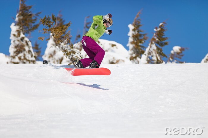 Fototapete Weiblicher Snowboarder springen auf Berghang