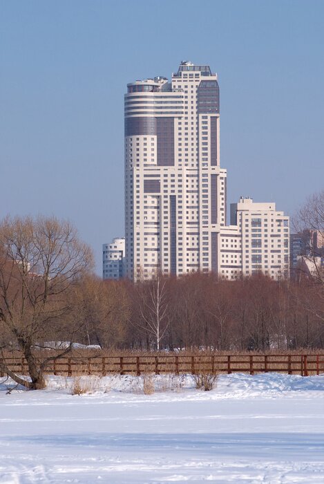 Fototapete Winterlandschaft mit modernen Hochhaus nach Wald