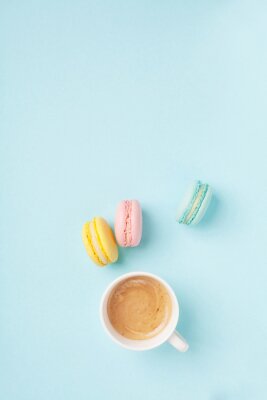 Poster Cup of coffee and colorful macaron on pastel blue background top view. Cozy morning breakfast. Fashion flat lay style. Sweet macaroons.