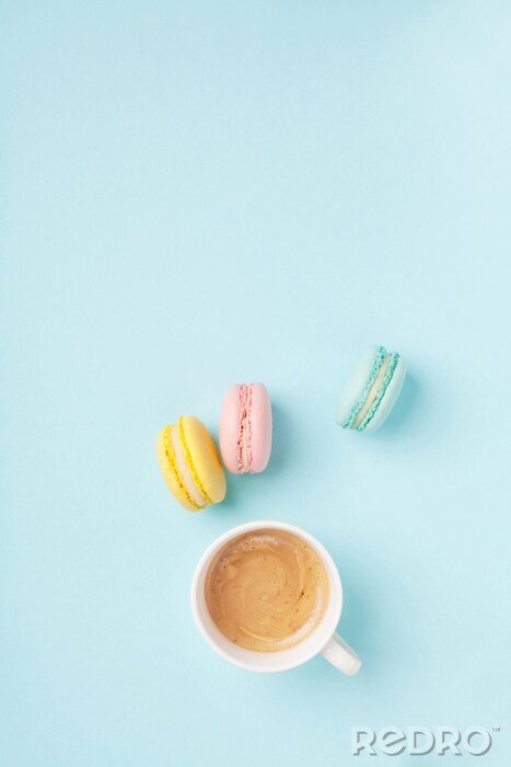 Poster Cup of coffee and colorful macaron on pastel blue background top view. Cozy morning breakfast. Fashion flat lay style. Sweet macaroons.