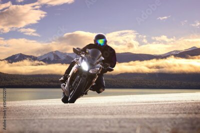 Poster Ein Motorradfahrer fährt vor der Kulisse von Bergen und Wolken.