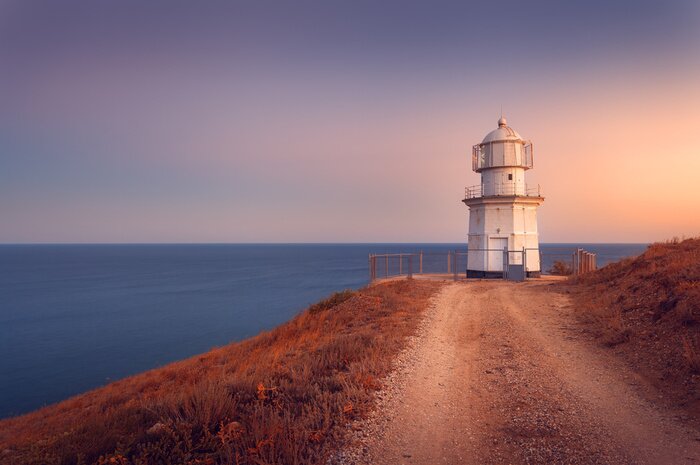 Poster Schöne weiße Leuchtturm auf der Ozean-Küste bei Sonnenuntergang. Lan