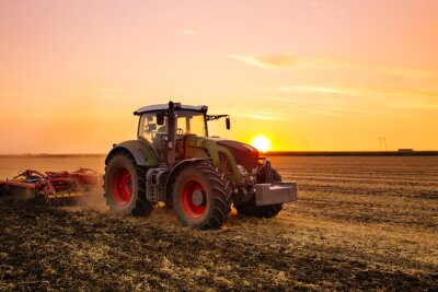 Poster Traktor auf einem Feld bei Sonnenuntergang