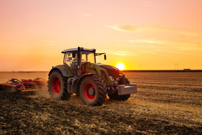 Poster Traktor auf einem Feld bei Sonnenuntergang